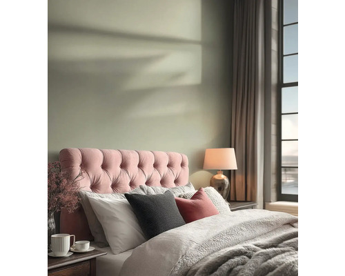 Helles Schlafzimmer mit einem rosa gesteppten Kopfteil, hellgrüner Wandfarbe, gemütlicher Bettwäsche und einer Tischlampe.