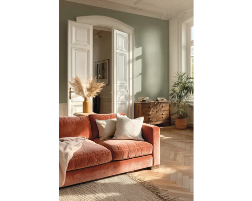 Helles Wohnzimmer mit salbeigrüner Wand, terrakottafarbenem Samtsofa, Holzkommode, Fischgrätparkett und einer großen Zimmerpflanze.