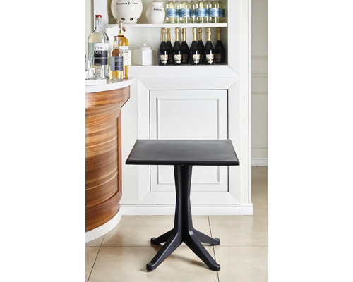 Schwarzer quadratischer Bistrotisch aus Kunststoff mit einem Vierfußgestell in einem hellen, organisierten Innenraum neben einer hölzernen Theke.