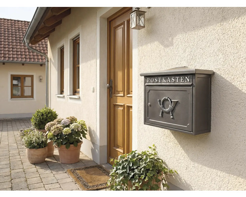 Grauer Briefkasten mit Hornmotiv an einer Hauswand neben einer Haustür.