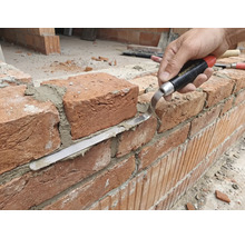 Handwerker bearbeitet Ziegelwand mit Fugenkelle