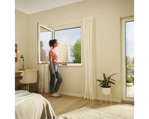 Helles Schlafzimmer mit Kippfenster und einer Frau, die nach draußen schaut