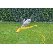 Hund springt über einen gelben Wassersprinkler in Schlangenform auf einer Rasenfläche.