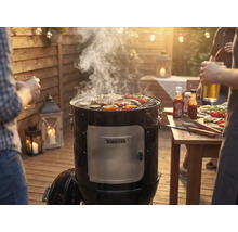 Rauchgrill mit Fleisch und Gemüse auf dem Grillrost bei einer Grillparty im Garten.