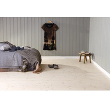 Schlafzimmer mit hellem Boden in Holzoptik, grauer Wandverkleidung aus Holzpaneelen, Bett mit Decken und rustikalem Holzhocker.