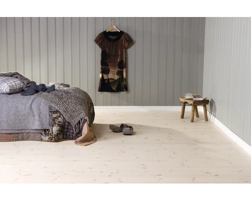 Schlafzimmer mit hellem Boden in Holzoptik, grauer Wandverkleidung aus Holzpaneelen, Bett mit Decken und rustikalem Holzhocker.