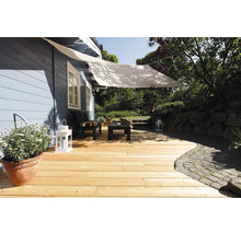 Holzterrasse mit hellen Dielen, weißem Sonnensegel, schwarzen Gartenmöbeln und Laternen vor einem blauen Holzhaus im Garten.