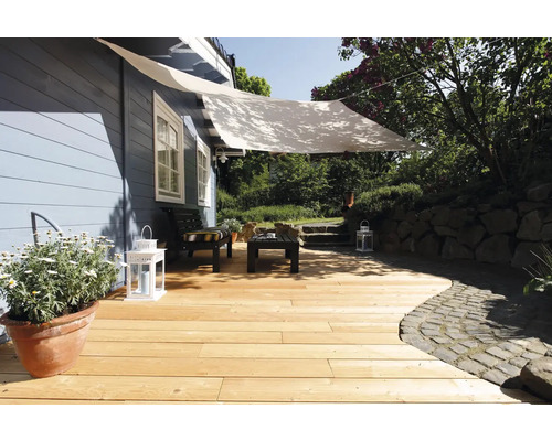 Holzterrasse mit hellen Dielen, weißem Sonnensegel, schwarzen Gartenmöbeln und Laternen vor einem blauen Holzhaus im Garten.