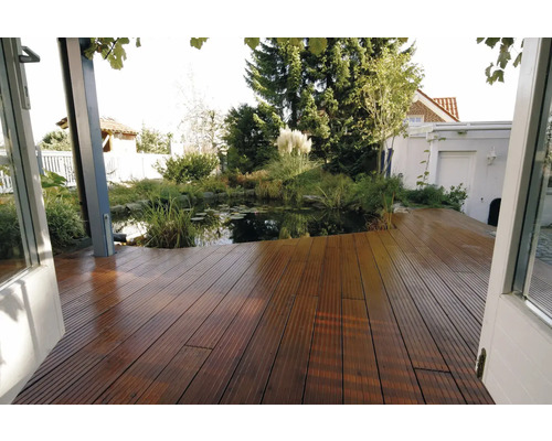 Holzterrasse aus geriffelten Dielen mit Blick auf einen Gartenteich mit Seerosen und üppiger Bepflanzung im Hintergrund.