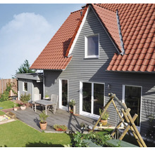Haus mit grauer horizontaler Fassadenverkleidung, rotem Ziegeldach und einer Holzterrasse mit Tisch, Stühlen und Topfpflanzen neben einer Rasenfläche.