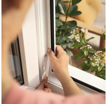 Eine Person montiert eine Fensterdichtung an einem weißen Fensterrahmen.