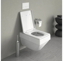 Wandhängendes WC mit offenem Spülrand, Betätigungsplatte, Toilettenpapierhalter und WC-Bürstengarnitur in einem Badezimmer.