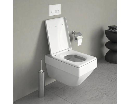 Wandhängendes WC mit offenem Spülrand, Betätigungsplatte, Toilettenpapierhalter und WC-Bürstengarnitur in einem Badezimmer.