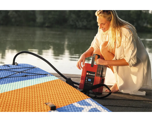 Frau pumpt ein Stand Up Paddle Board mit einer Einhell Luftpumpe auf einem Holzsteg auf