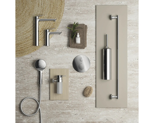 Anordnung moderner verchromter Badezimmerarmaturen wie Waschtischmischer, Handbrause, Duschsteuerung, Seifenspender und Toilettenbürstenhalter auf Stein