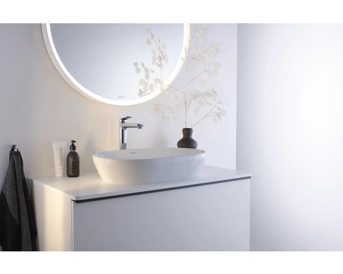 Helles Badezimmer mit weißem Aufsatzwaschbecken, verchromter Armatur, hellem Waschtischunterschrank und rundem LED-Spiegel.