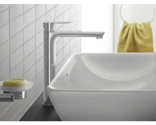 Moderne, hohe Waschtischarmatur in Chrom an einem weißen Aufsatzwaschbecken in einem hellen Badezimmer mit weißen Fliesen.