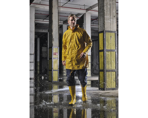 Mann in gelber Regenjacke und Gummistiefeln in einer Industriehalle