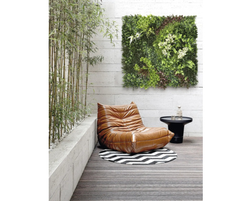 Szene mit einem Sessel, einem Tisch, einem runden Teppich und einem grünen Wandpaneel auf einer Terrasse