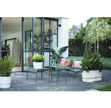 Moderne Terrasse mit grüner Gartenbank aus Metall, Beistelltischen und weißen Blumentöpfen vor einer Glasfront.