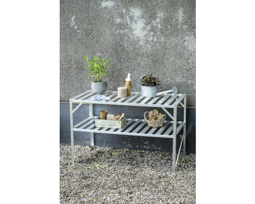 Zweistöckiges Gartenregal aus Aluminium mit Pflanzen und Gartenwerkzeugen auf einer Kiesfläche.