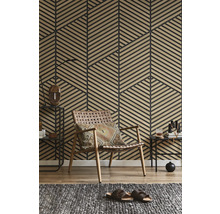 Wand mit geometrischen Holzlamellen-Paneelen in einem Wohnzimmer mit geflochtenem Ledersessel und grauem Teppich.