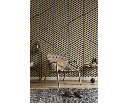 Wand mit geometrischen Holzlamellen-Paneelen in einem Wohnzimmer mit geflochtenem Ledersessel und grauem Teppich.