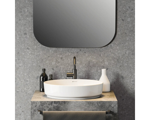 Modernes Badezimmer mit rundem weißem Aufsatzwaschbecken, schwarzer Armatur, Wand in Terrazzo-Optik und Spiegel mit abgerundeten Ecken.