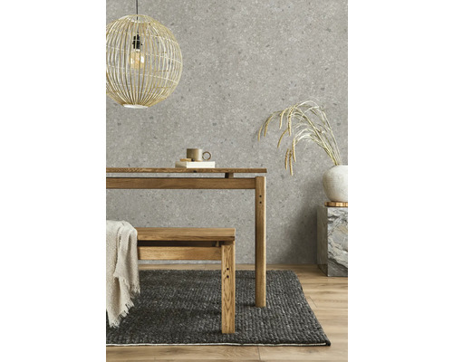 Vliestapete mit Steinoptik in Grau, kombiniert mit einem Holztisch, einer Holzbank, einem dunklen Webteppich und einer Korb-Hängeleuchte.