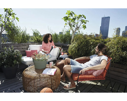 Entspannte Dachterrasse mit Loungemöbeln, einem Flechttisch aus Rattan und verschiedenen Topfpflanzen vor einer städtischen Skyline.