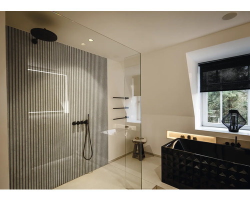 Modernes Badezimmer mit begehbarer Glasdusche, Wandpaneelen in Lamellenoptik, schwarzen Armaturen und einer strukturierten schwarzen Badewanne.