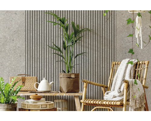 Modern gestalteter Wohnraum mit Akustikpaneelen, Wand in Steinoptik, Zimmerpflanzen und einem Sessel aus Rattan.