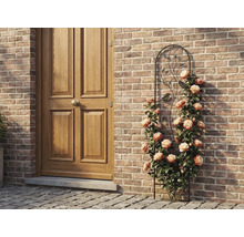 Rankgitter aus Metall mit Vogel- und Blattmotiven, bewachsen mit Kletterrosen an einer Mauer aus Ziegelsteinen neben einer Holztür.