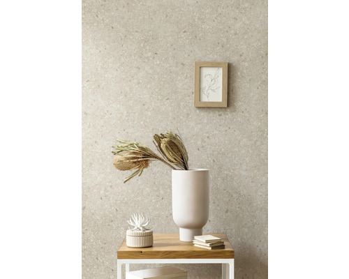 Vliestapete in Steinoptik mit Terrazzo-Muster in einem Wohnraum kombiniert mit einer weißen Vase, Trockenblumen und einem Holzrahmen.