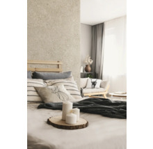 Helles Schlafzimmer mit Wand in Natursteinoptik, Holzbett, gestreiften Kissen und weißen Kerzen auf einer Holzscheibe.