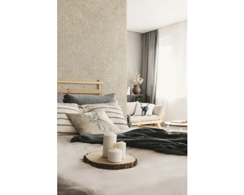 Helles Schlafzimmer mit Wand in Natursteinoptik, Holzbett, gestreiften Kissen und weißen Kerzen auf einer Holzscheibe.