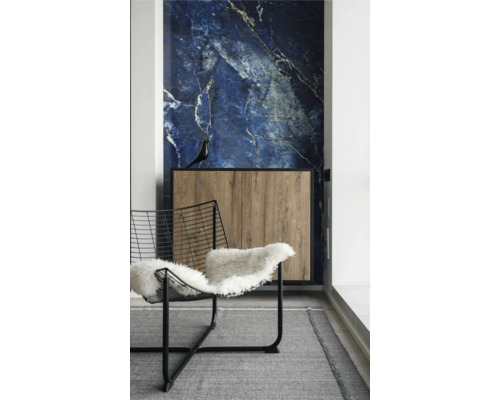 Innenraum mit blauer Marmor-Wandverkleidung, Holz-Sideboard mit schwarzem Rahmen und Drahtstuhl mit weißem Fell auf grauem Teppich.