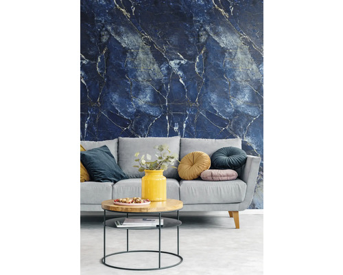 Vliestapete mit dunkelblauem Marmormuster und hellen Adern in einem modern eingerichteten Wohnzimmer mit grauem Sofa und Holztisch.