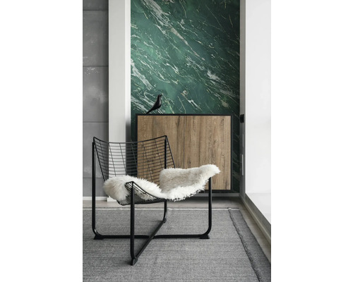 Modernes Zimmer mit grüner Marmortapete, schwarzem Drahtsessel mit weißem Fell und Sideboard in Holzoptik auf grauem Teppich.