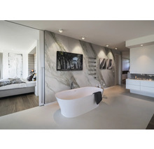 Modernes Badezimmer mit freistehender weißer Badewanne vor Marmorwand, Wandbildern, Handtuchhalter und heller Beleuchtung.