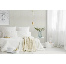 Helles, minimalistisches Schlafzimmer mit weißem Bett, Strickdecke, Seil-Pendelleuchte, transparenten Vorhängen und Beistelltisch mit Glasvase.