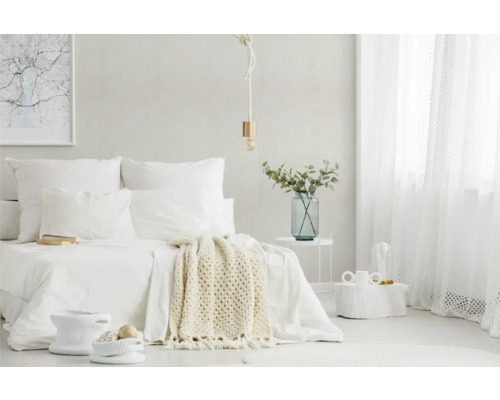 Helles, minimalistisches Schlafzimmer mit weißem Bett, Strickdecke, Seil-Pendelleuchte, transparenten Vorhängen und Beistelltisch mit Glasvase.