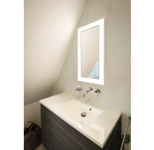 Moderner Waschtisch mit dunklem Unterschrank, weißem Waschbecken, verchromter Wandarmatur und beleuchtetem Spiegel in hellem Badezimmer.