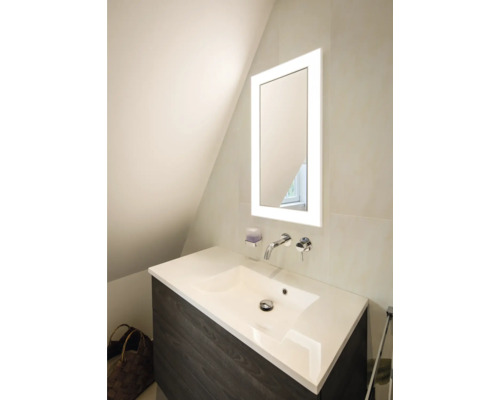 Moderner Waschtisch mit dunklem Unterschrank, weißem Waschbecken, verchromter Wandarmatur und beleuchtetem Spiegel in hellem Badezimmer.