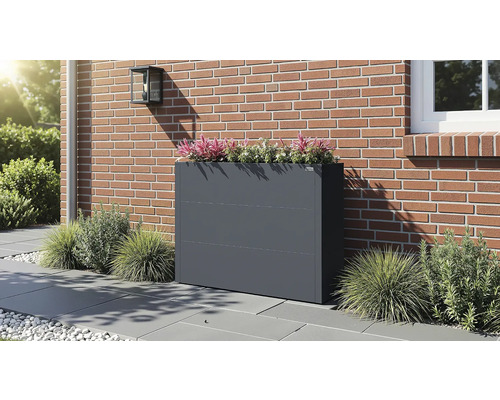 Anthrazitfarbener Pflanzkübel aus Metall auf einer Terrasse vor einer Backsteinwand, bepflanzt mit Zierpflanzen.