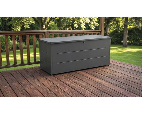 Dunkelgraue Gartenbox aus Metall auf einer Holzterrasse mit Geländer vor einem Garten.