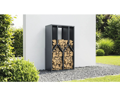 Anthrazitfarbenes Kaminholzregal aus Metall, gefüllt mit Brennholz, in einem Garten auf Kies vor einer Wand.