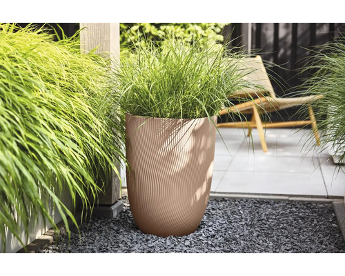 Beiger Pflanzkübel mit Wellenstruktur und Ziergras auf einer modernen Terrasse mit grauem Kies.