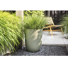 Moderner, hoher Pflanzkübel mit vertikaler Wellenstruktur und Ziergras auf einer hellen, organisierten Terrasse mit Kies und Bodenplatten.