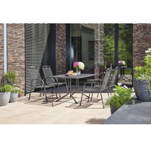 Vier Gartenstühle aus grauem Streckmetall stehen um einen passenden Tisch auf einer hell gepflasterten Terrasse vor einer Klinkerwand.